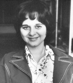 [Image description: This black-and-white headshot pictures Julie Cochran-Rogers with short dark hair, wearing a white floral blouse and dark jacket.]