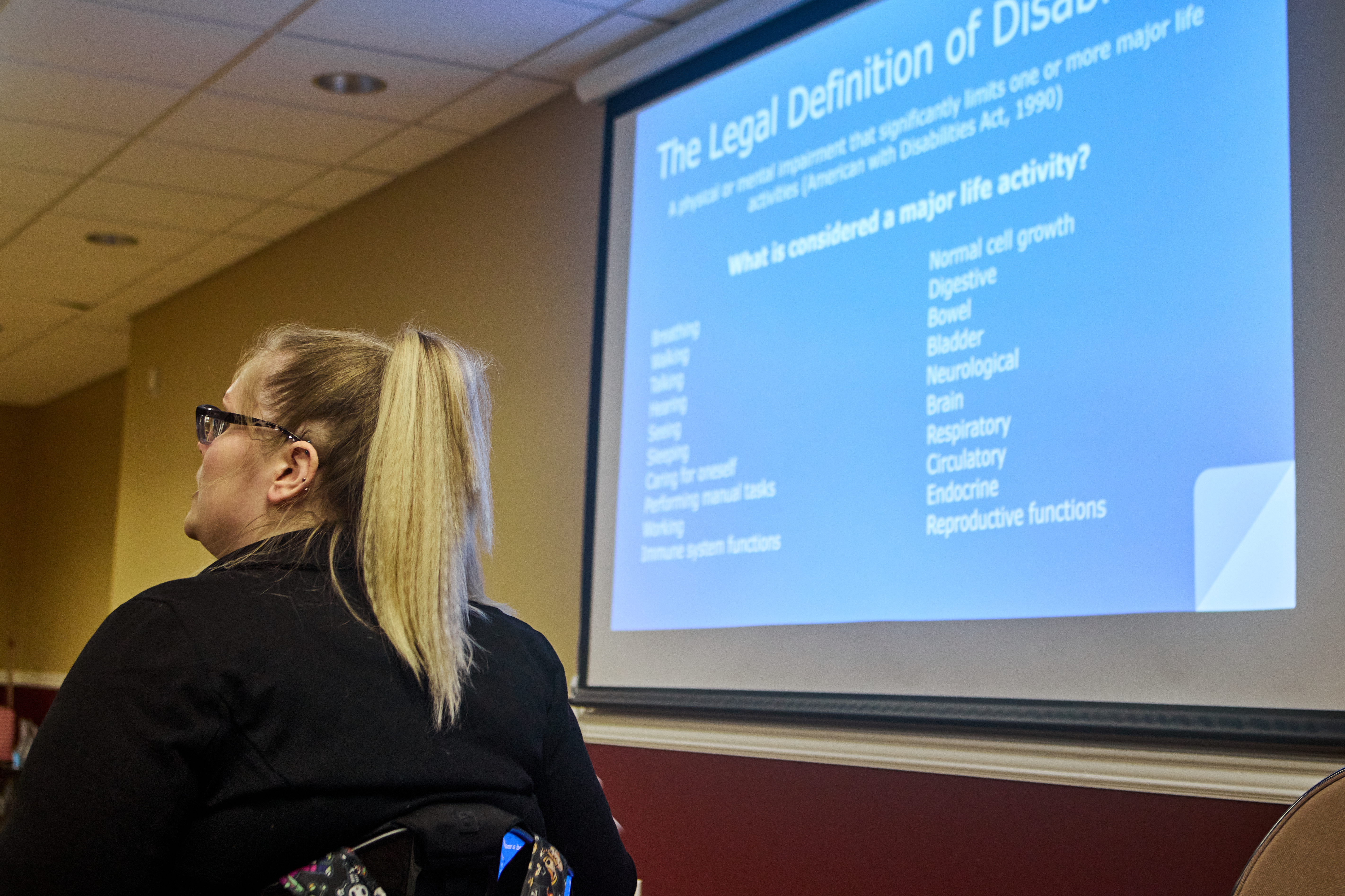 [Image description: Barb sitting in front of a screen projecting, "the legal definition of disability."]