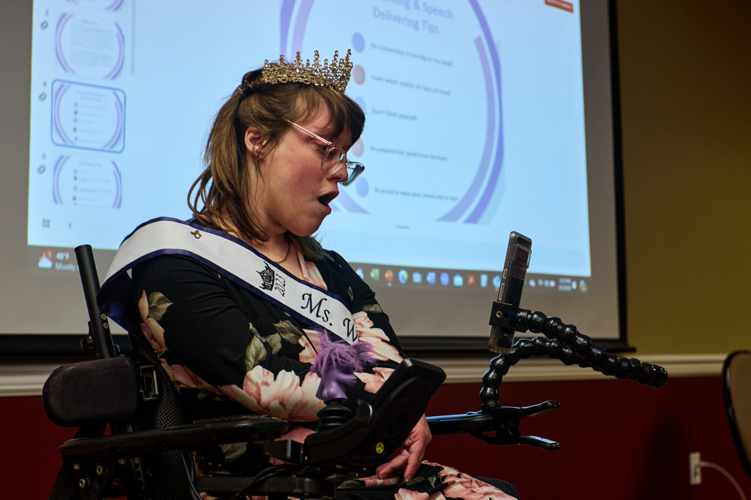 [Image description: Former Ms. Wheelchair Ohio 2023, Allison Boot, wearing her sash and crown, sitting in front of a screen projecting tips for the 2024 contestants.]

