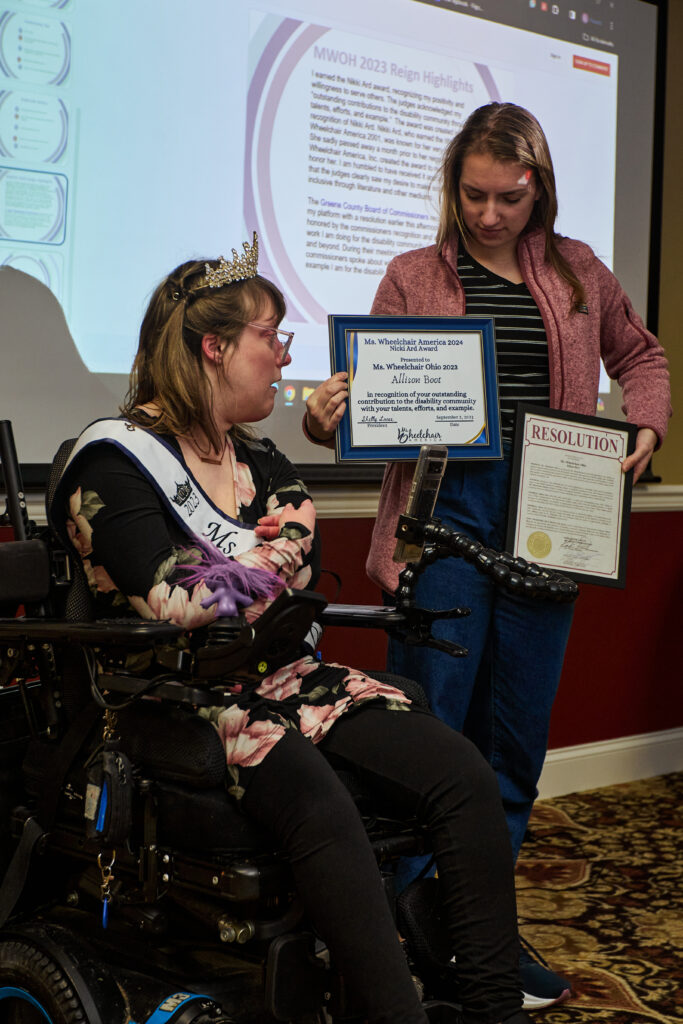 [Image description: Allison with her caregiver, presenting certificates Allison earned during her reign.]