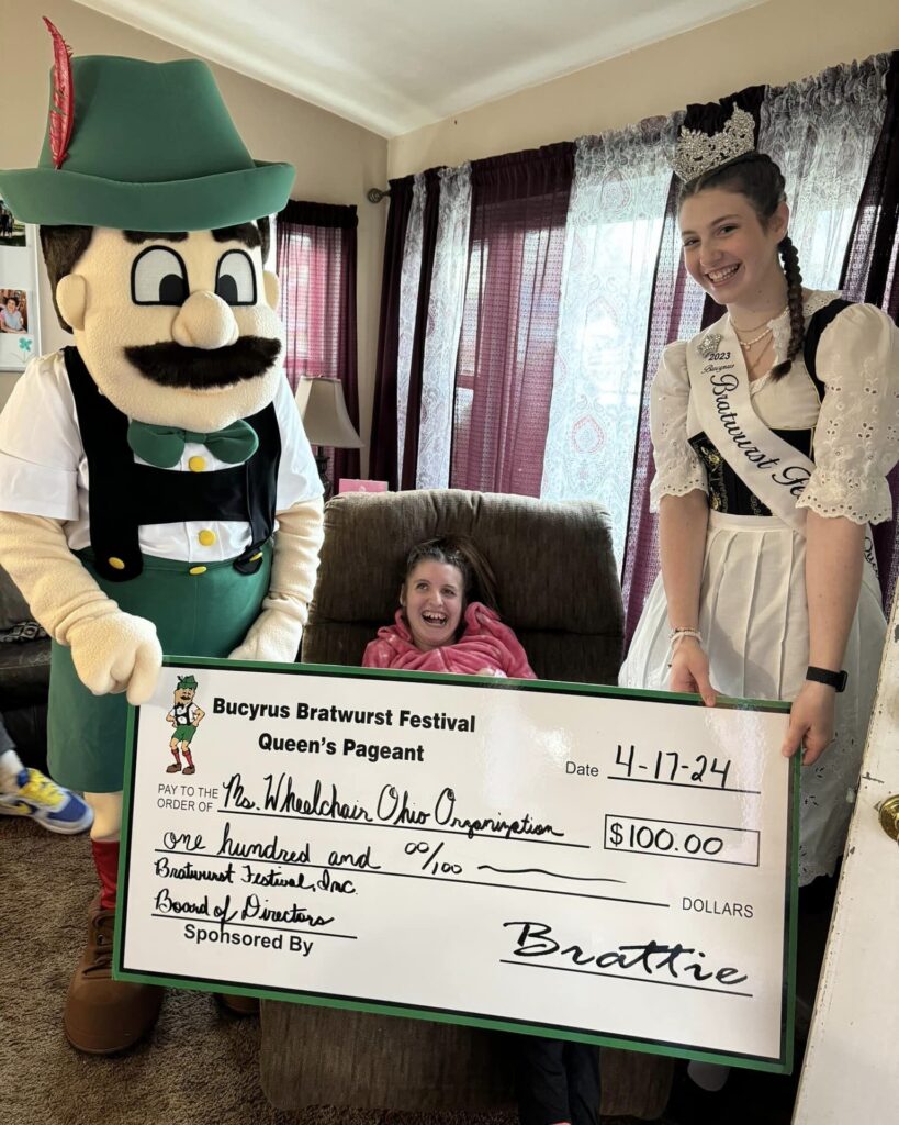 Gabby sits in a recliner between the Bratwurst Festival Queen and Brattie the mascot. They hold a large $100 check presented to the Ms. Wheelchair Ohio Organization.
