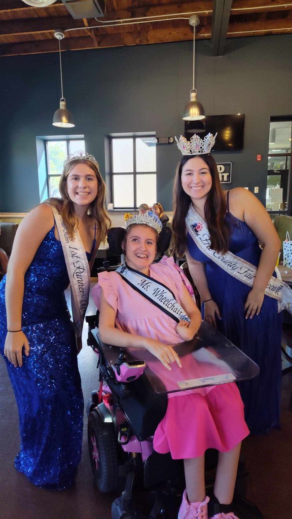 Gabby is wearing her sash and crown sitting between two young women. The women are also wearing crowns and sashes that represent their 2024 titles.